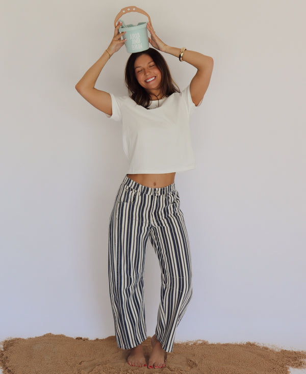 Person wearing a white top and striped pants holding a small bucket against a plain background