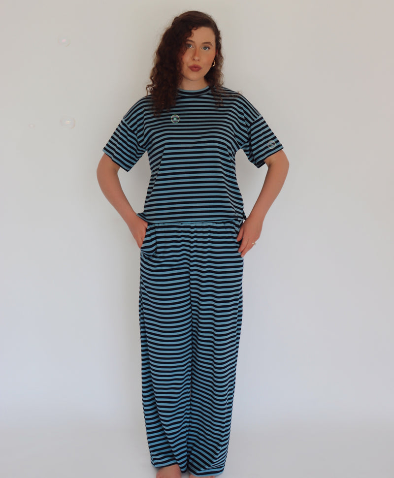 A woman modeling a matching two-piece loungewear set consisting of a short-sleeve crewneck top and wide-leg pants, both featuring horizontal dark teal and navy stripes.