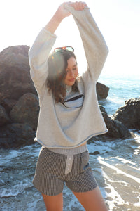 Woman outdoors by a rocky coastline, wearing a gray fish sweater and black shorts. 
