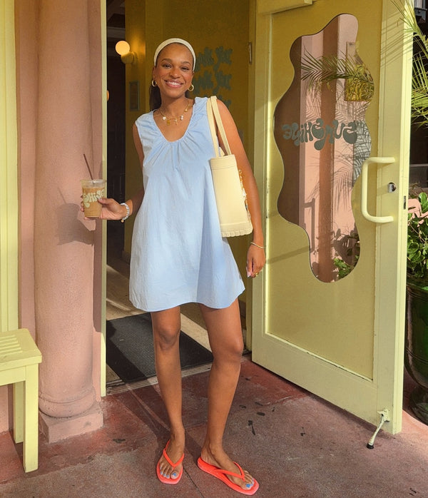Woman in a light blue dress holding a coffee outside.