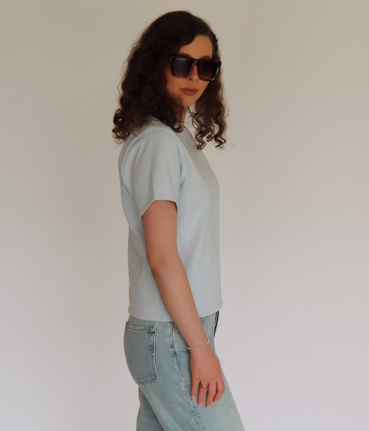 Woman wearing a light blue tee shirt and denim in front of a white background 