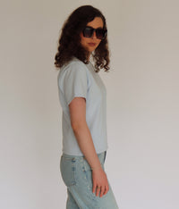 Woman wearing a light blue tee shirt and denim in front of a white background 