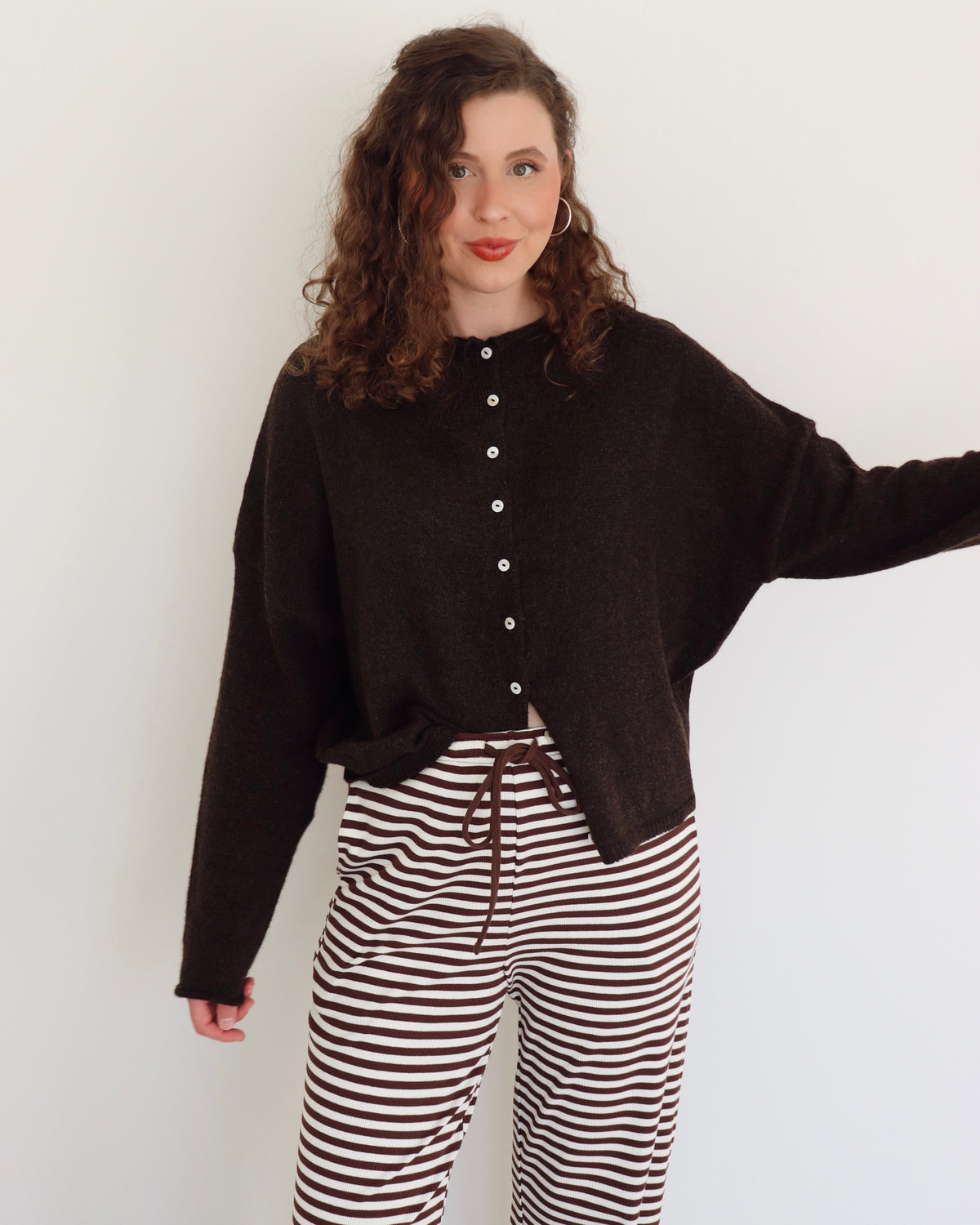 Woman wearing a chocolate brown cardigan and striped pants against a white background