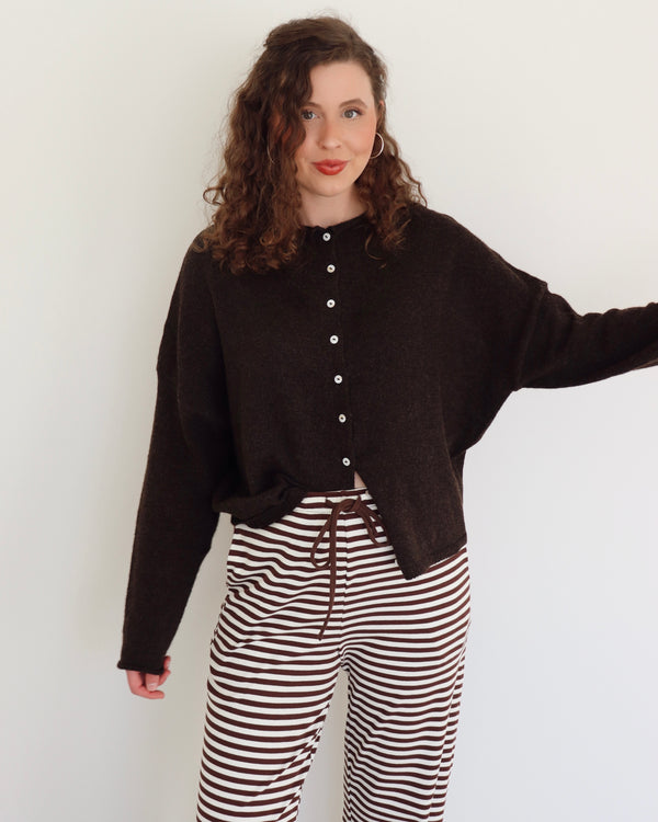 Woman wearing a chocolate brown cardigan and striped pants against a white background