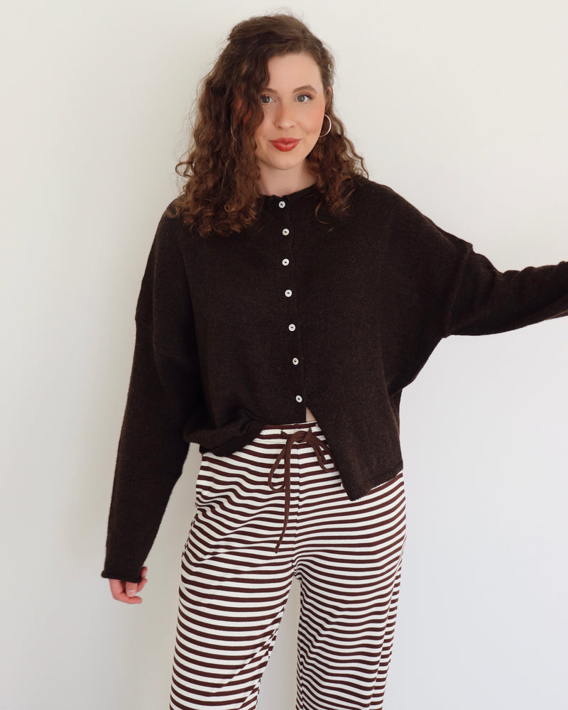 Woman wearing a chocolate brown cardigan and striped pants against a white background