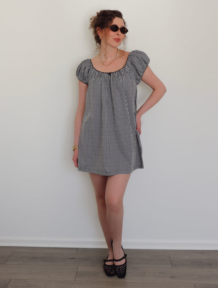 Woman wearing a black and white checkered dress against a white wall.