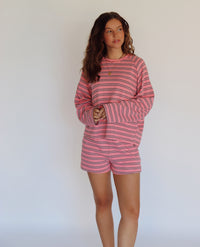 A woman modeling a pink and brown striped lounge set consisting of a long-sleeve top and matching shorts, posed against a plain white studio background.