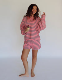 A woman modeling a pink and brown striped lounge set consisting of a long-sleeve top and matching shorts, posed against a plain white studio background.