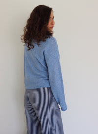 Person wearing a blue henley and striped pants against a plain background