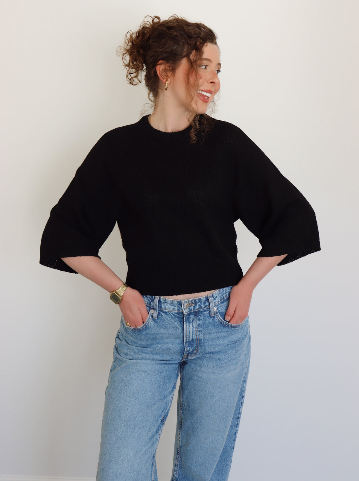 Person wearing a black top and blue jeans against a plain background