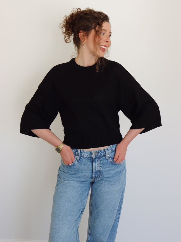 Person wearing a black top and blue jeans against a plain background