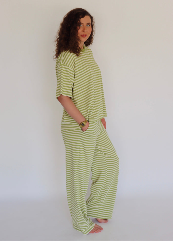 A woman modeling a light green and white horizontally striped two-piece lounge set consisting of a short-sleeve top and matching wide-leg pants, standing against a plain white studio background.
