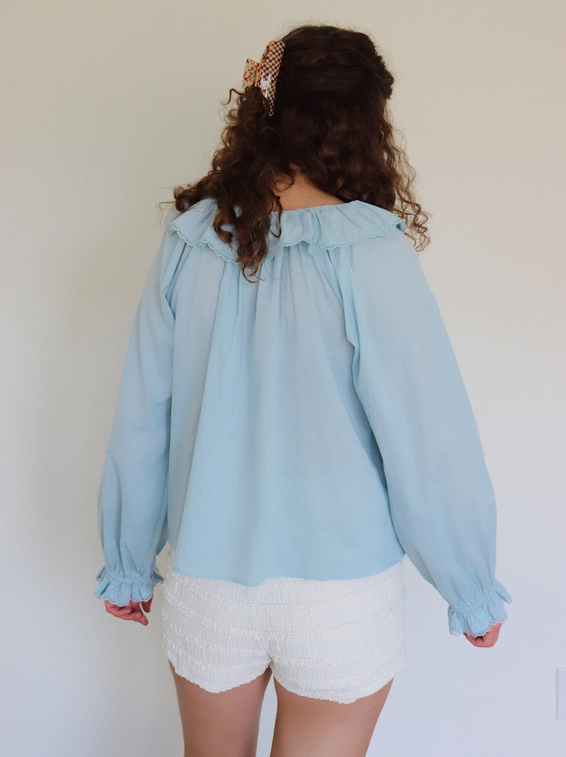 Woman wearing a light blue ruffled collar top and white shorts