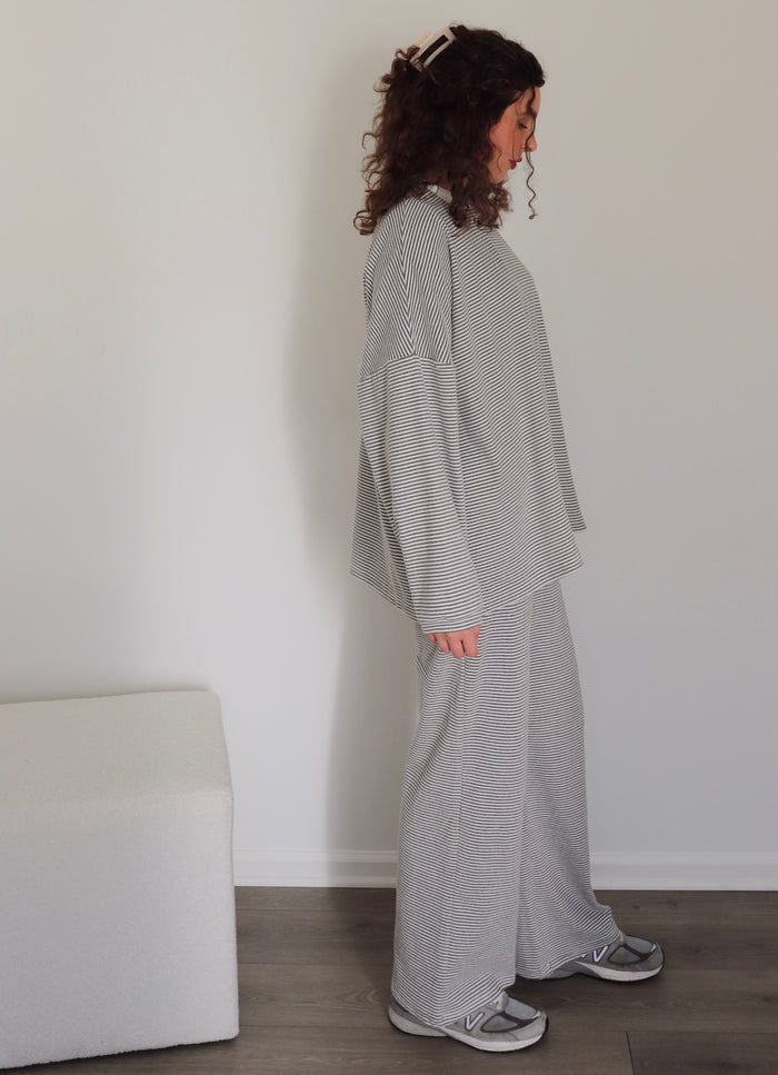 Woman wearing a gray striped outfit standing against a white wall.