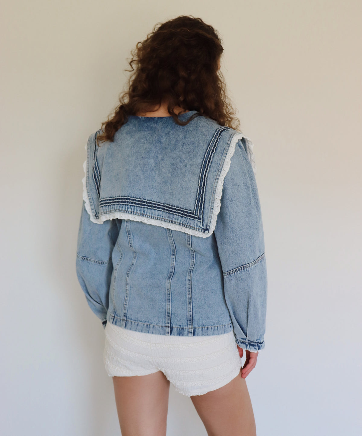 woman wearing a detailed denim jacket with white shorts 