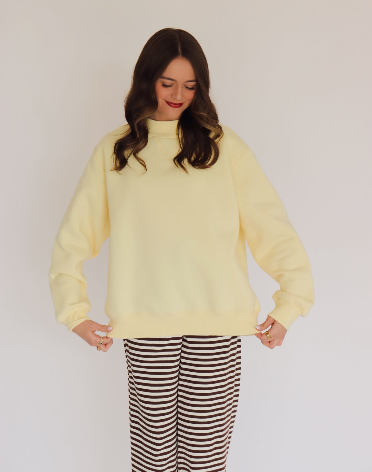 Woman wearing a light yellow pullover and striped pants against a plain background
