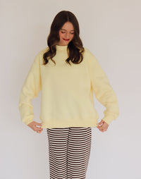 Woman wearing a light yellow pullover and striped pants against a plain background