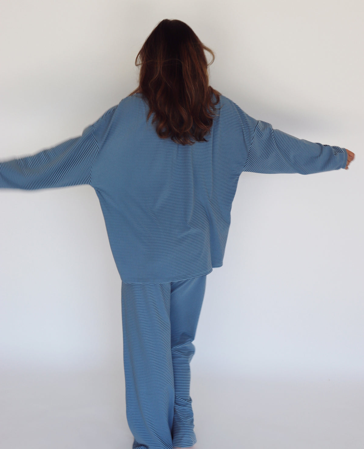 A woman modeling a matching blue striped lounge set, consisting of a long-sleeve top and wide-leg pants, against a plain white studio background.