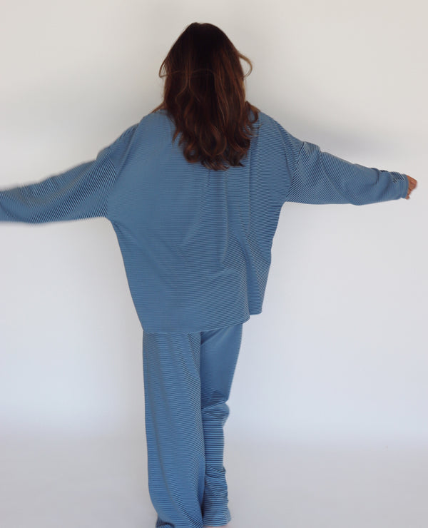 A woman modeling a matching blue striped lounge set, consisting of a long-sleeve top and wide-leg pants, against a plain white studio background.