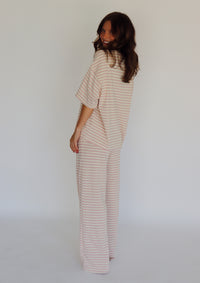 A woman modeling a matching two-piece loungewear set with short-sleeve top and wide-leg pants, featuring horizontal stripes in a light pink and off-white color, set against a plain white studio background.