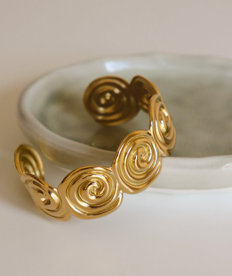 Gold bracelet with spiral design on a light green  dish