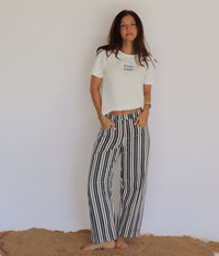 Woman wearing a white t-shirt and striped pants standing against a plain background