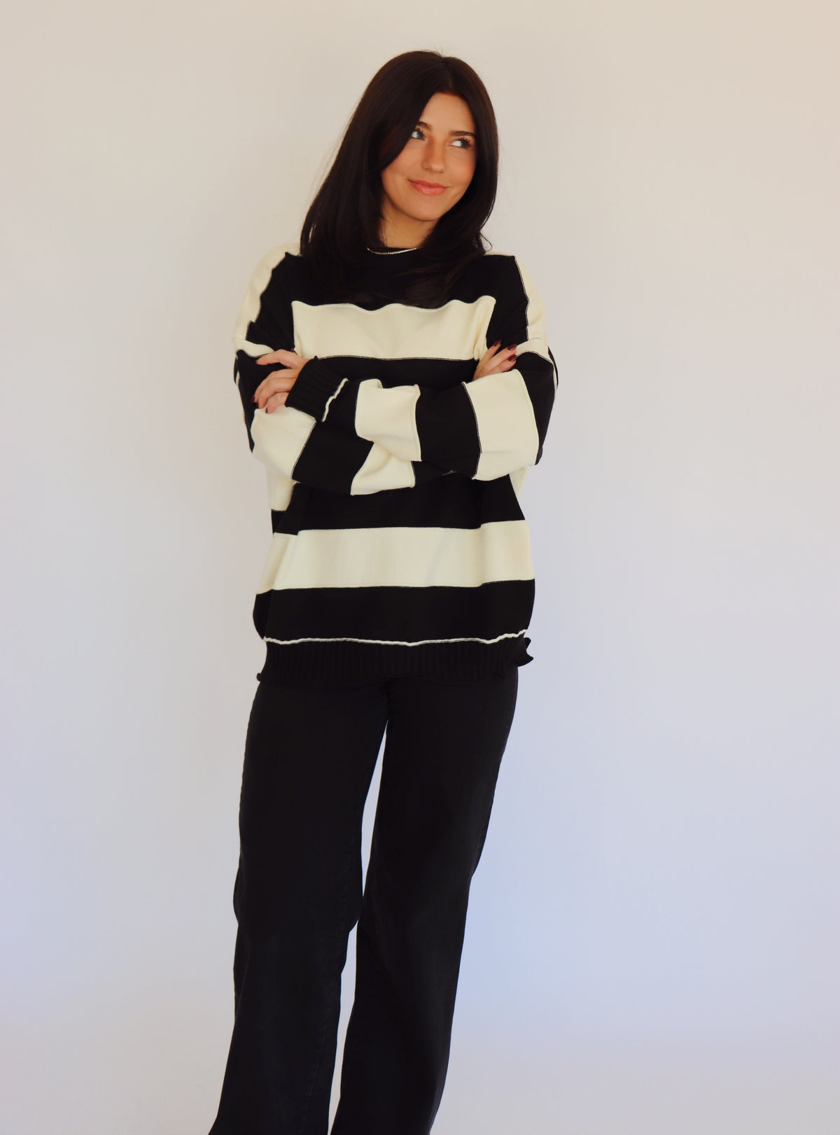 Person wearing a black and white striped pullover and black jeans against a plain background
