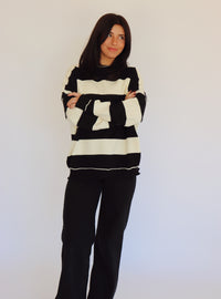 Person wearing a black and white striped pullover and black jeans against a plain background