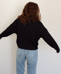 Person wearing a black cardigan and light blue jeans against a white background