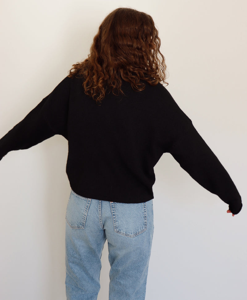 Person wearing a black cardigan and light blue jeans against a white background