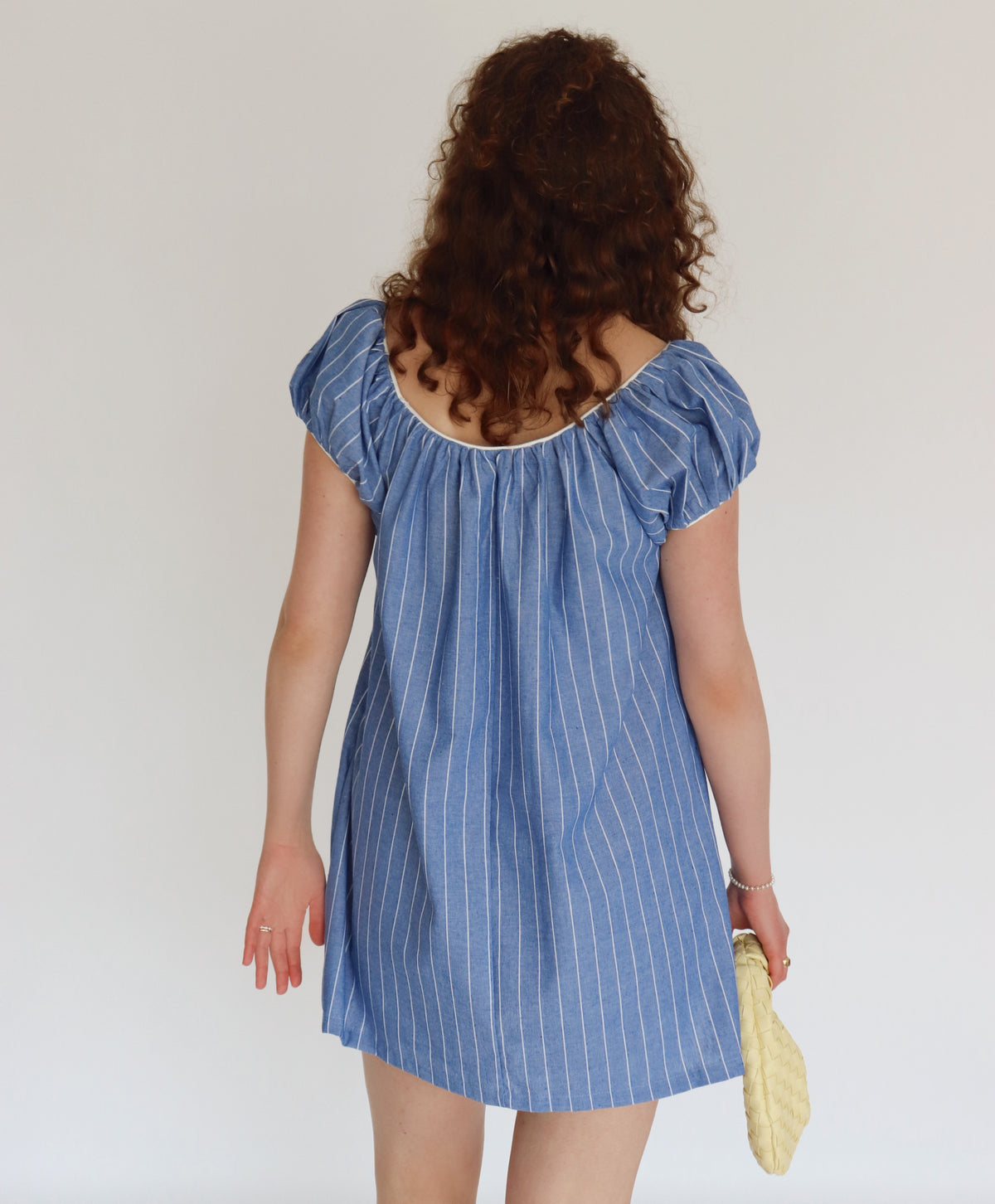 Woman wearing a blue striped dress holding a yellow bag against a plain background