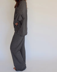 A woman modeling a matching two-piece loungewear set consisting of a long-sleeve top and wide-leg pants, both featuring a navy and white horizontal stripe pattern, set against a plain white studio background.
