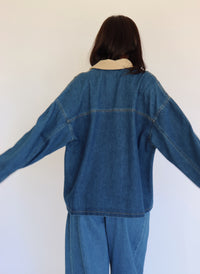 Person wearing a blue denim jacket and denim pants against a white background