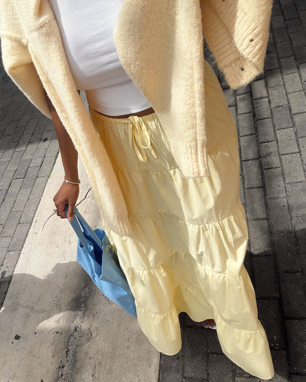 Person wearing a yellow outfit with a white top and blue bag on a sidewalk.