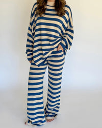 A woman wearing a matching two-piece loungewear set with blue and beige horizontal stripes, featuring a long-sleeve top and wide-leg pants, standing against a plain white background.