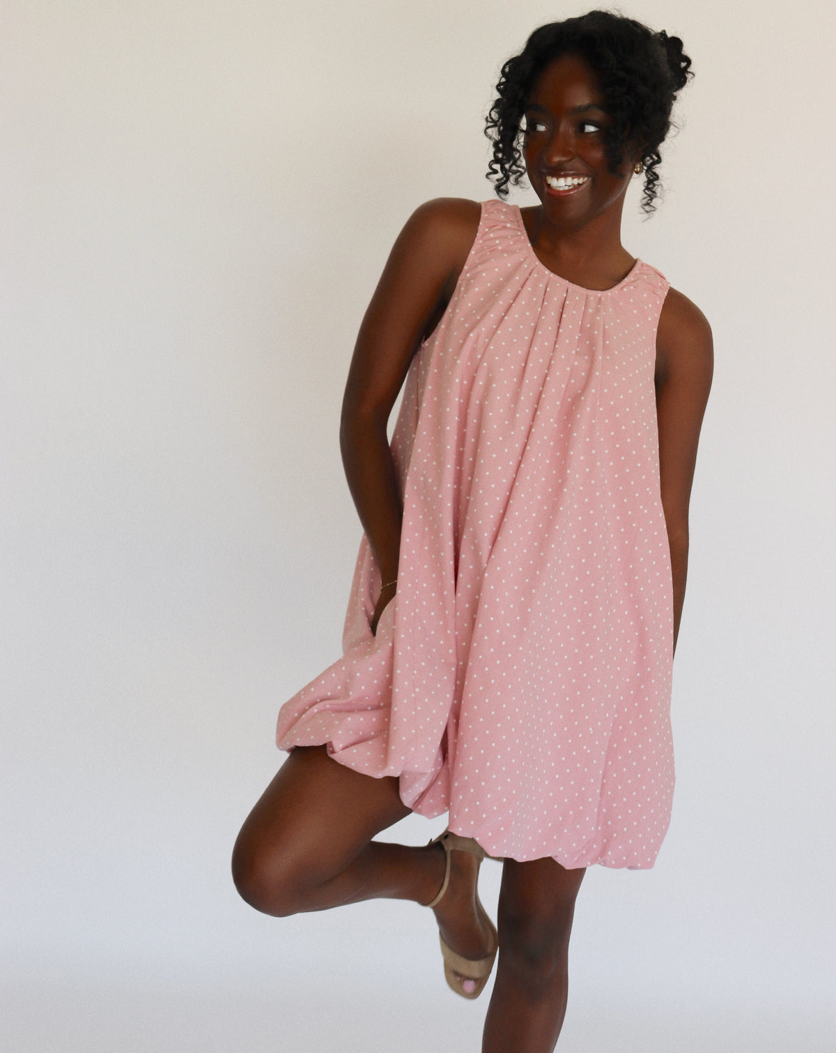 Woman wearing a pink dress with white polka dots on it against a white background