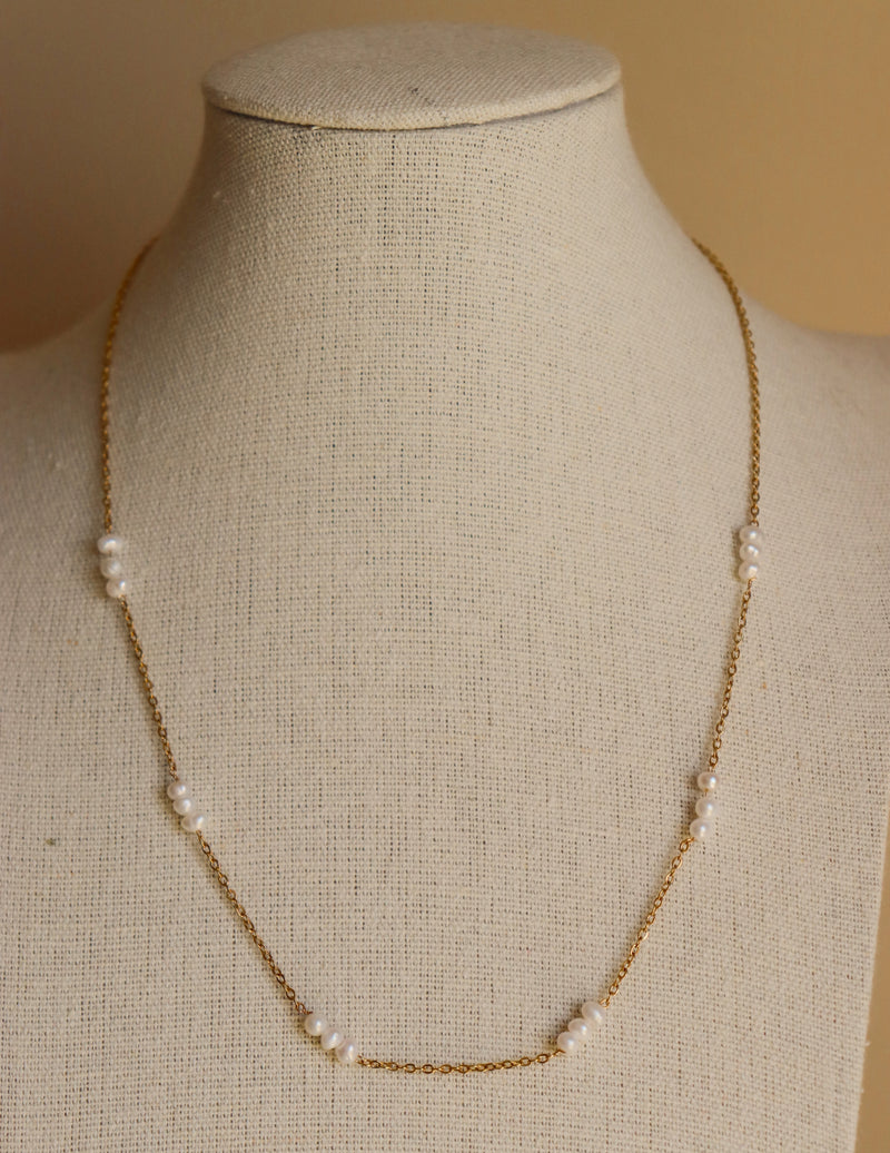 Gold necklace with pearls on a mannequin bust against a beige background