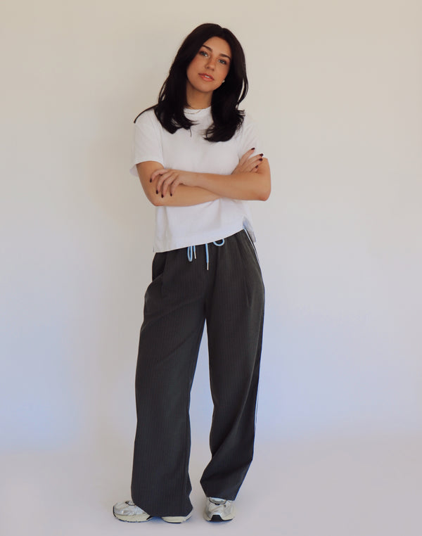 Person wearing dark gray pants and a white shirt against a plain background