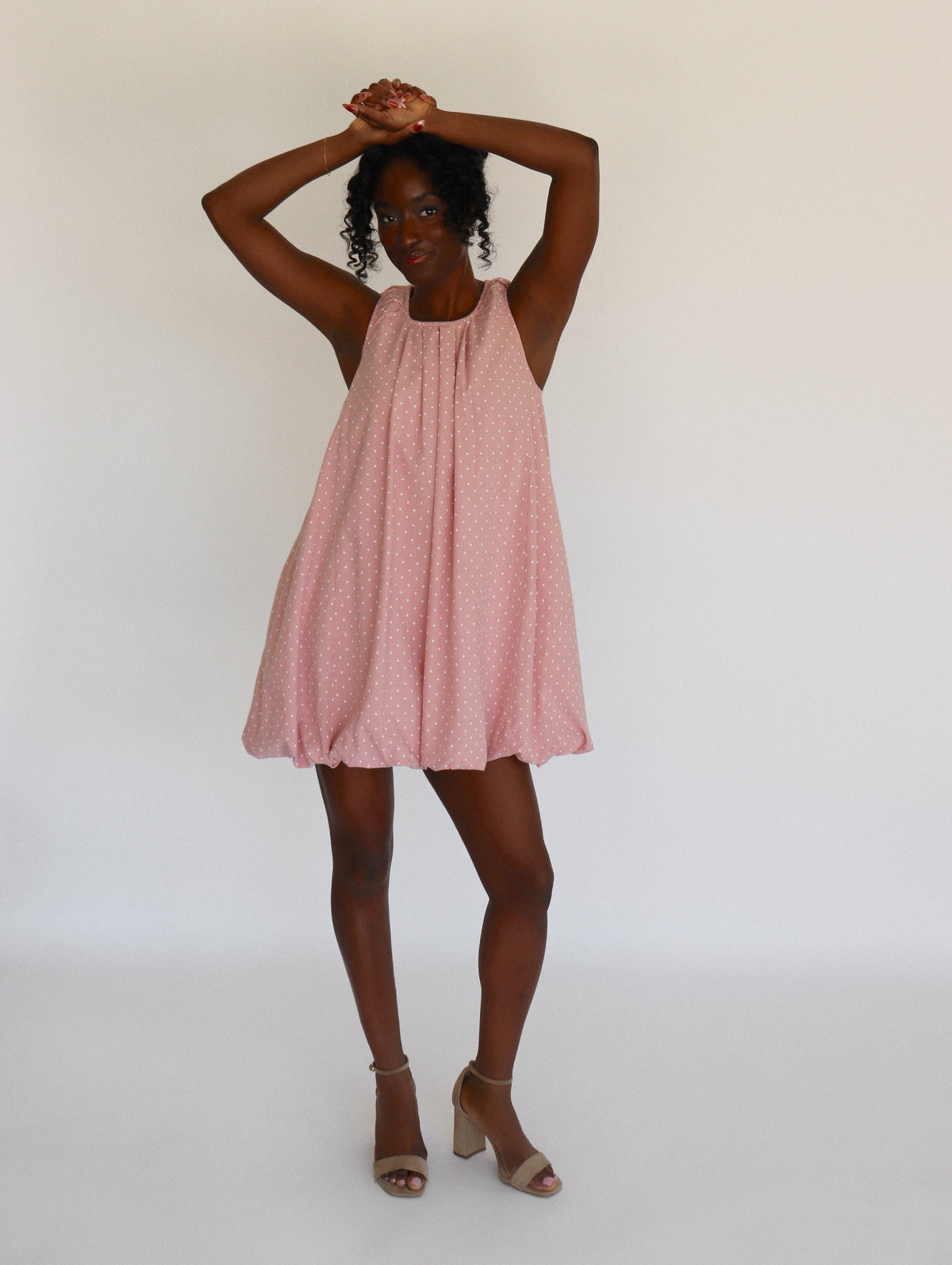 Woman wearing a pink dress with white polka dots on it against a white background