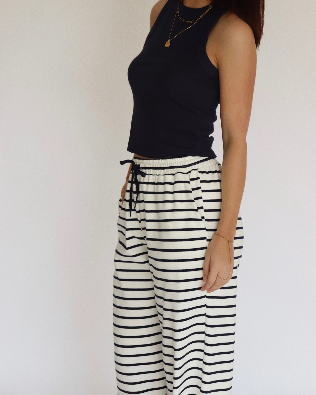 Woman wearing a navy blue sleeveless top and striped pants against a plain background