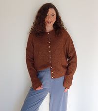 Woman wearing a brown cardigan over blue and brown striped pants against a plain background.