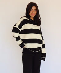 Person wearing a black and white striped pullover and black jeans against a plain background