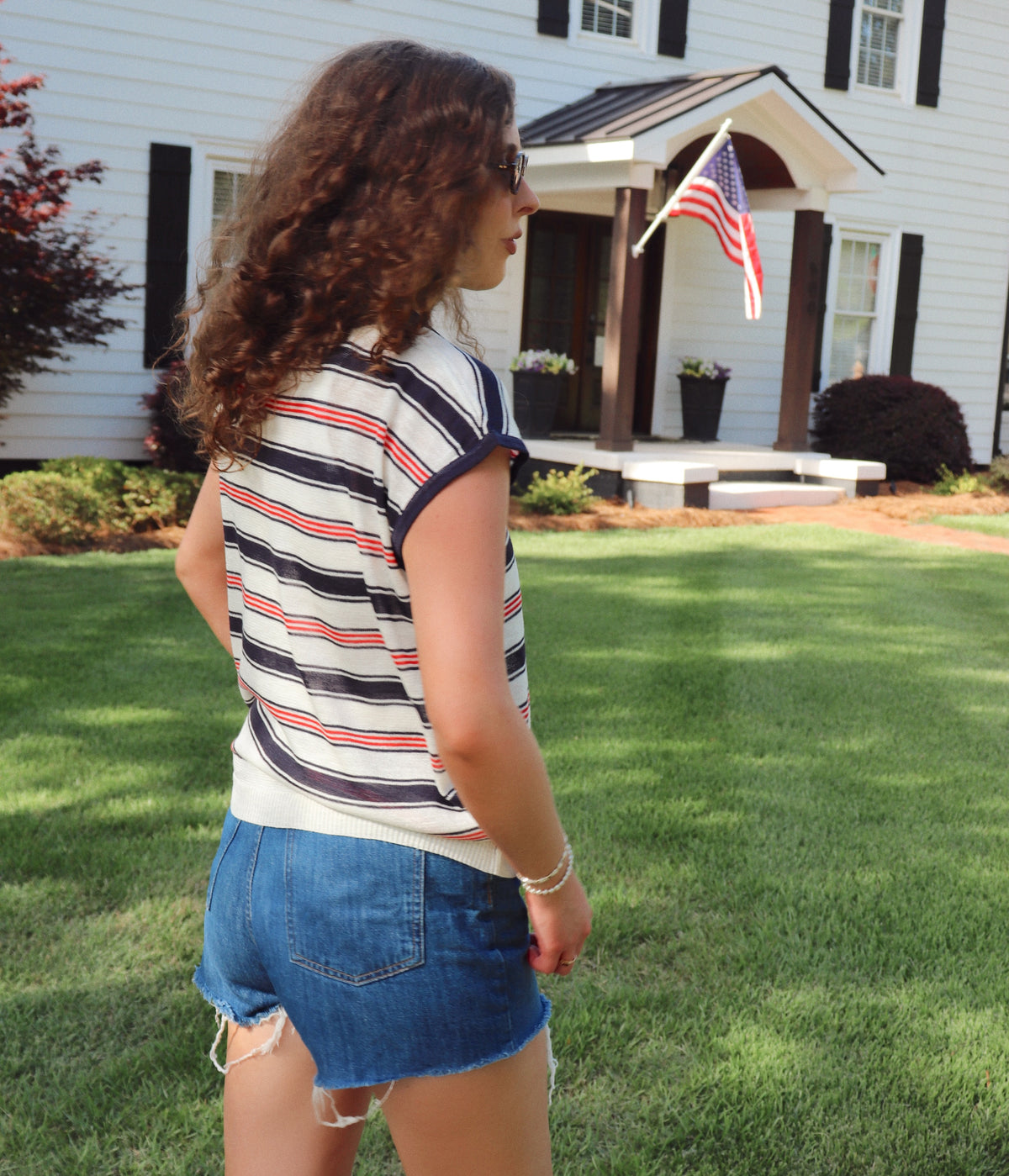 Woman wearing a striped shirt and denim shorts standing in front of a house