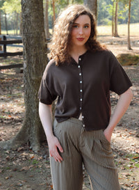 a woman wearing a chocolate brown short sleeve cardigan with brown striped pants stands in an outdoor setting