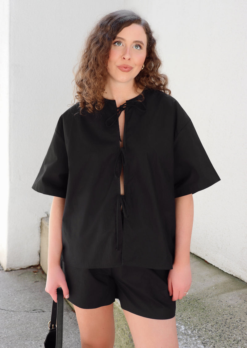Woman in a black outfit standing on concrete background against a beige  wall.