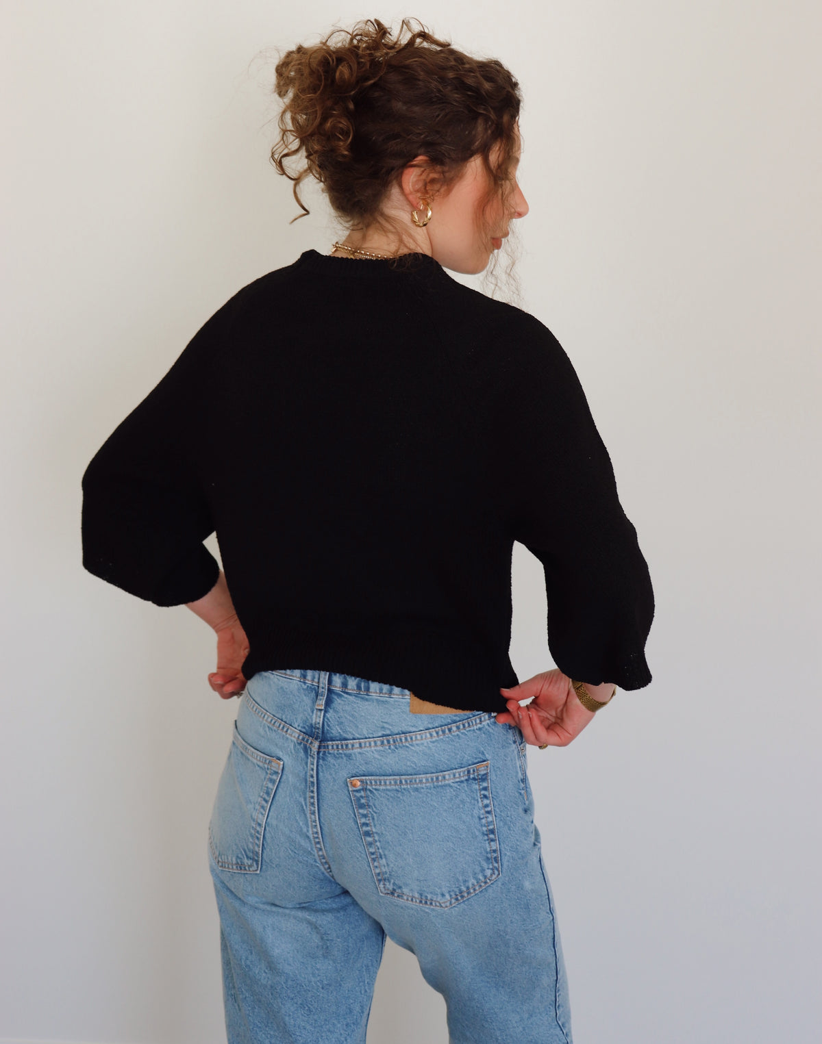 Person wearing a black top and blue jeans against a plain background