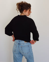 Person wearing a black top and blue jeans against a plain background