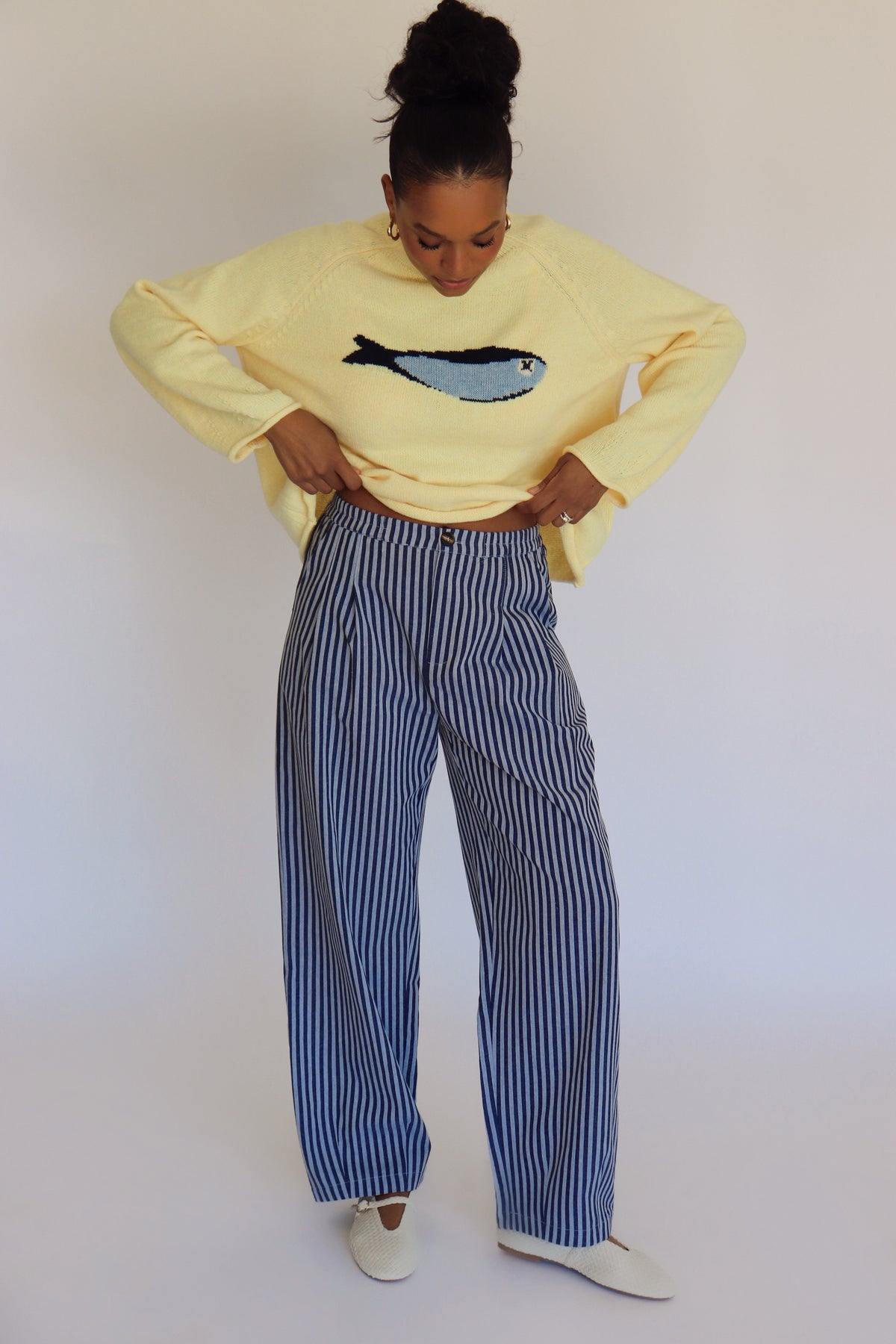 Person wearing a light yellow sweater with a fish design and striped pants against a plain background