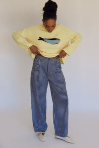 Person wearing a light yellow sweater with a fish design and striped pants against a plain background