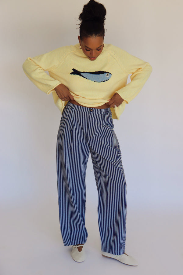 Person wearing a light yellow sweater with a fish design and striped pants against a plain background